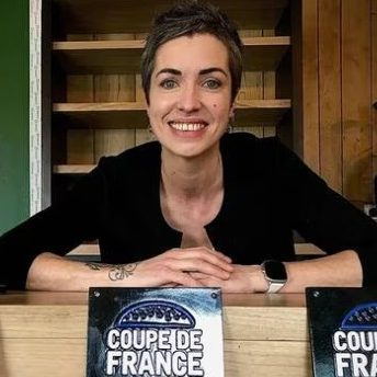 Une cheffe souriante présente un burger sur une assiette avec de la salade.