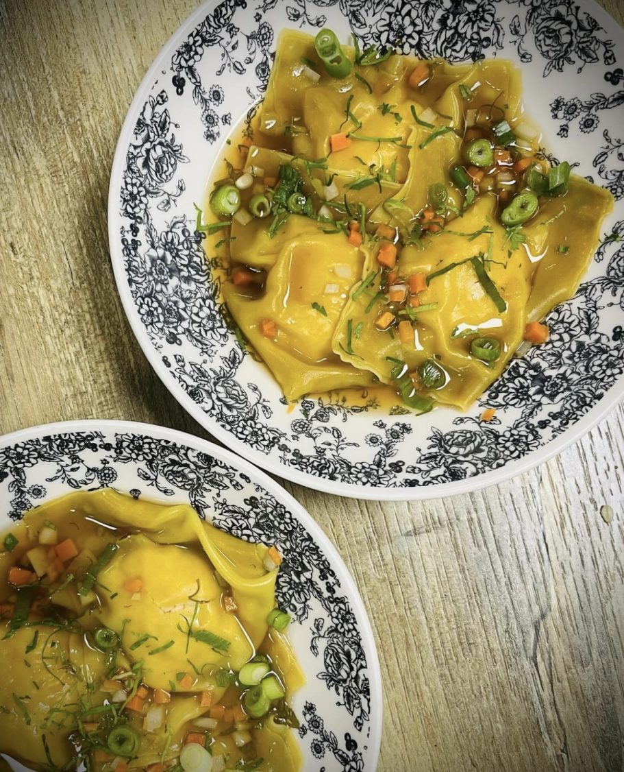 Raviolis en sauce, garnis d'oignons verts et de piment, servis dans des assiettes décoratives.