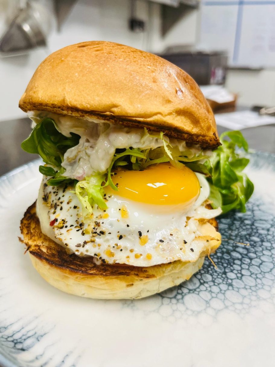 Burger avec un œuf au plat, laitue et sauce dans un petit pain doré.