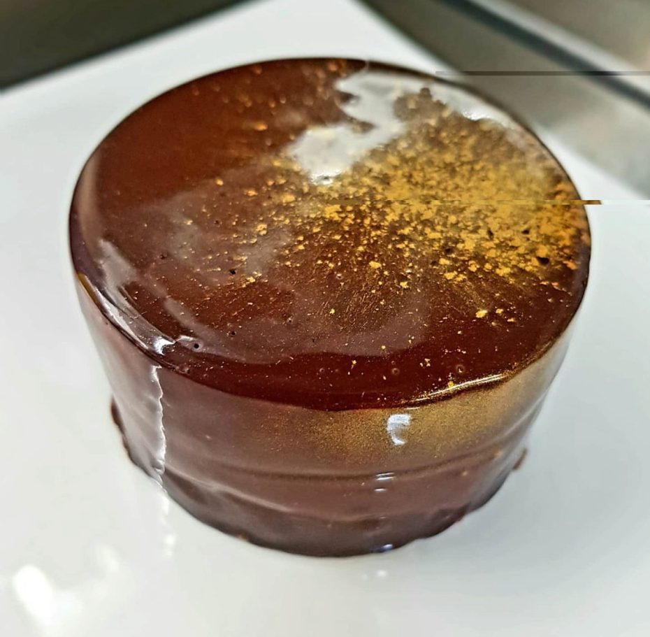 Gâteau glacé rond avec une finition brillante et des paillettes dorées sur le dessus.