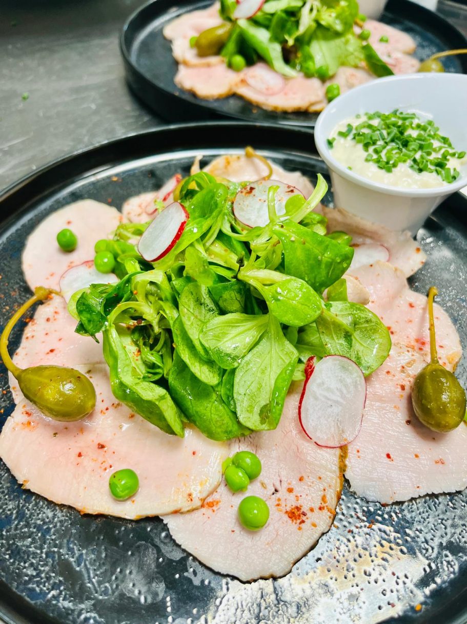 Assiette de charcuterie garnie de salade, radis, petits pois et sauce à côté.