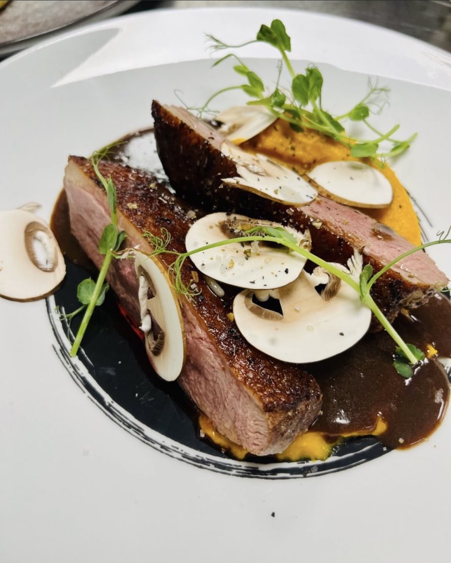 Tranche de viande avec sauce, purée et garniture de champignons et pousses.