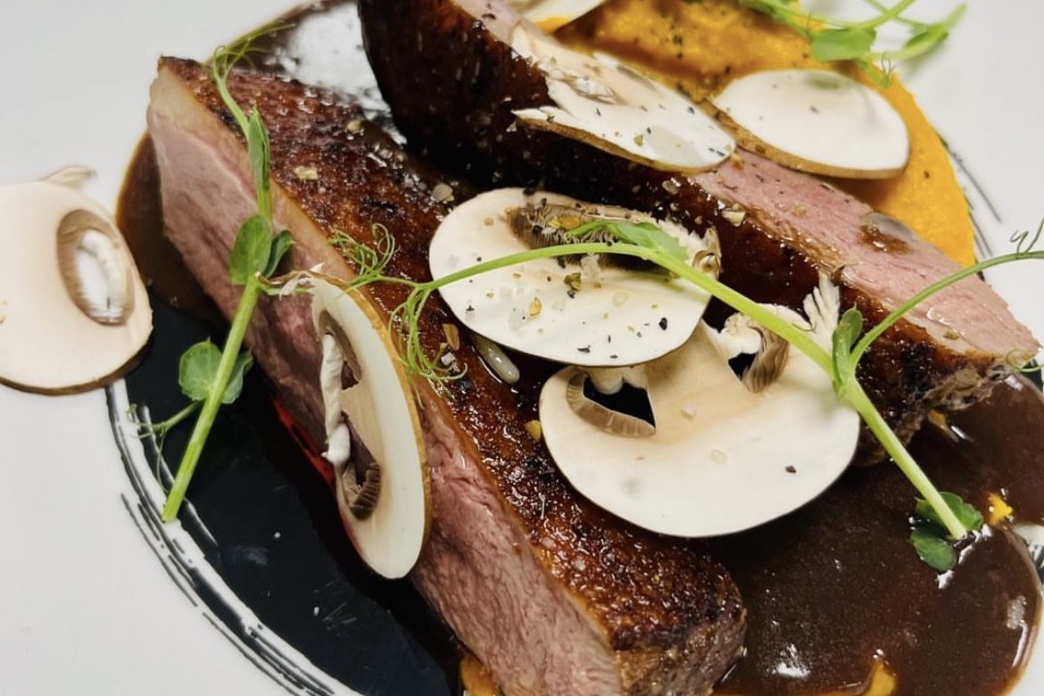 Tranche de viande, champignons tranchés, sauce brune et garniture verte.