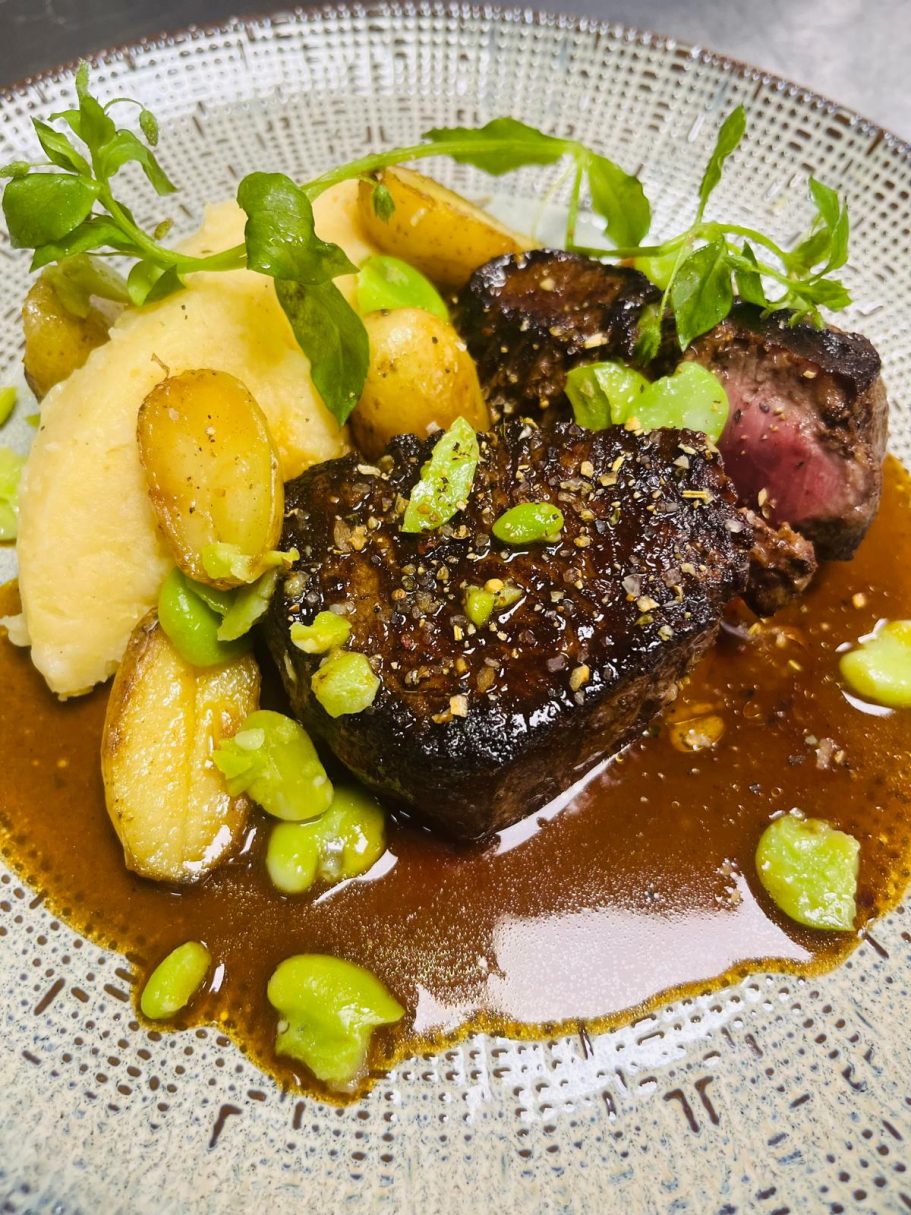 Plat de viande braisée avec purée, pommes de terre, et sauce, décoré d'herbes fraîches.